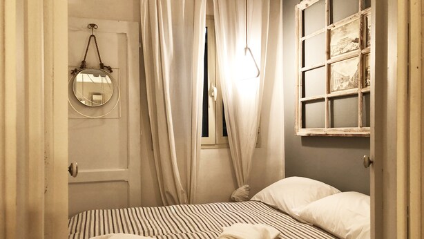 Ein Schlafzimmer mit gestreiftem Bettbezug, einem hängenden Spiegel und einem Fenster mit Vorhängen.