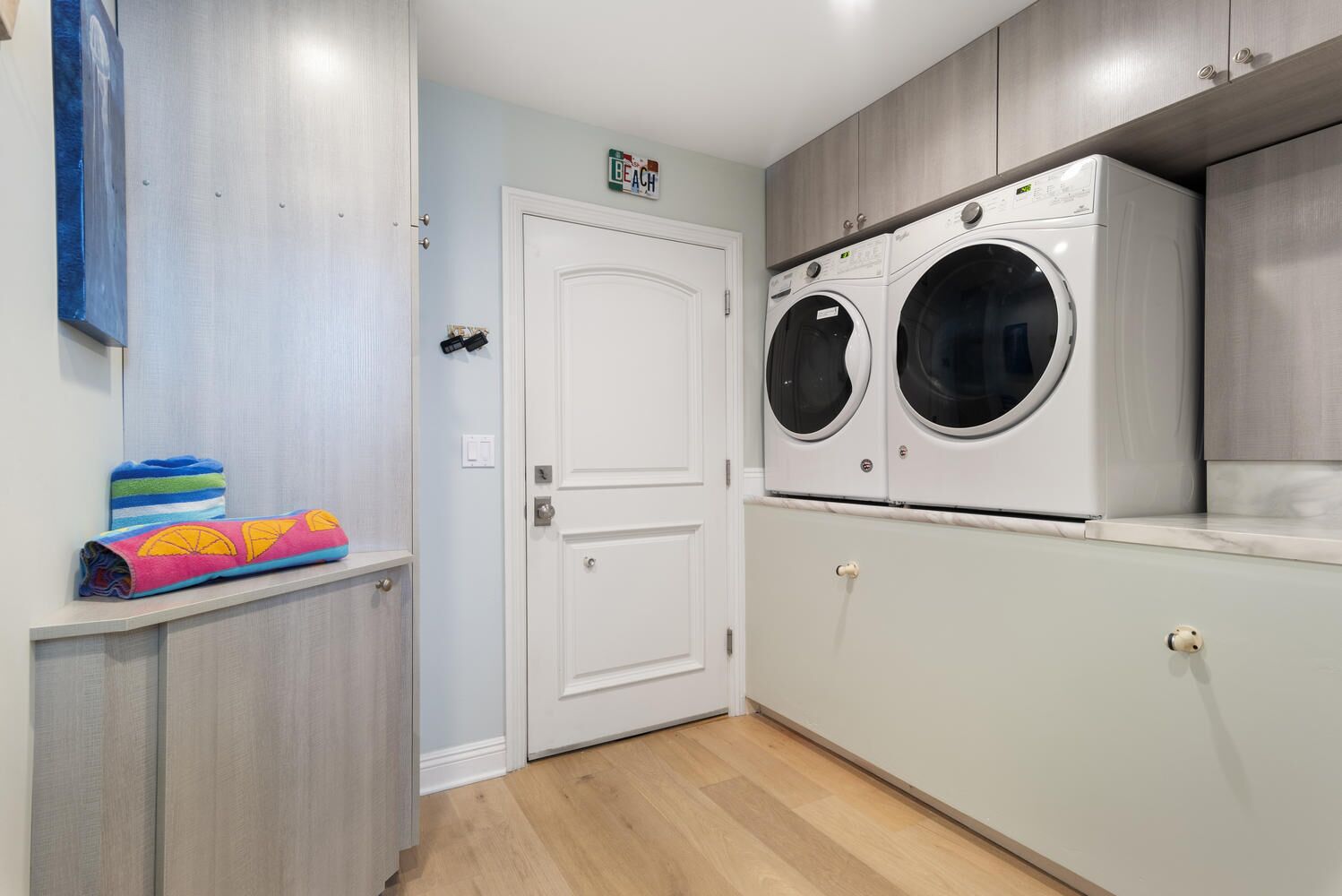 A laundry room with two stacked front-loading washing machines, a white door, and a shelf with folded towels.