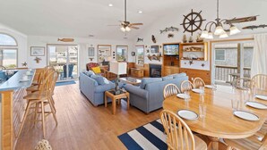 A spacious living area with a large sofa set, wooden dining table, and a kitchen area with a TV. - Semi-Oceanfront Dog Friendly Home in Avon w/ Pool, Hot Tub, Tiki Bar, Game Room (Avon)
