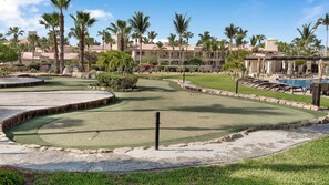 A golf course with a pool area, palm trees, and a building with a tiled roof.