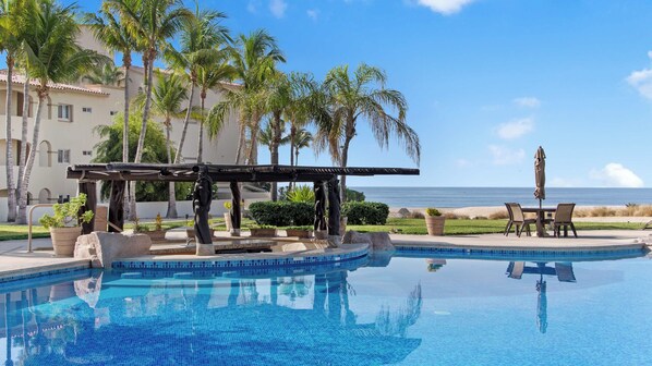 A swimming pool with a pergola, palm trees, and a view of the ocean.