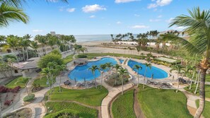 A resort with a large pool area, palm trees, and a view of the ocean.