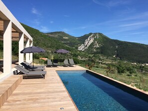 A poolside area with lounge chairs and umbrellas, overlooking a mountainous landscape.
