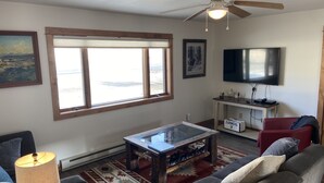 Un salon avec une grande fenêtre, un ventilateur de plafond, un téléviseur, une table basse et un canapé.
