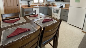 A kitchen with wooden cabinets, a refrigerator, a stove, and a dining table with placemats. - Yellowstone River View Condos, 10 min to Yellowstone Park on Historic Ranch (Gardiner)
