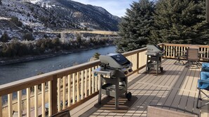 Une terrasse avec un barbecue et des chaises, donnant sur une rivière et des collines enneigées.