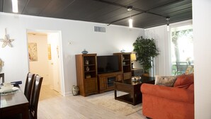 A living room with a wooden entertainment center, a sofa, and a dining area with chairs and a table. - Ft Walton cozy condo w/ on-site pool. Near beaches (Fort Walton Beach)