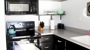 A kitchen with black cabinets, a microwave, a stove, and a checkered floor. - Ft Walton cozy condo w/ on-site pool. Near beaches (Fort Walton Beach)