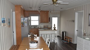 Une cuisine avec des meubles de rangement en bois, une table à manger avec des chaises, un réfrigérateur et un ventilateur de plafond.
