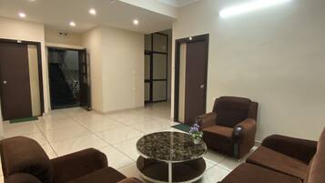 A spacious living area with a ceiling fan, a round coffee table with a vase of flowers, and brown armchairs.