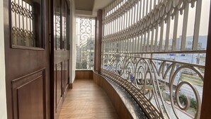 Un pasillo con suelo de madera, barandilla de metal con diseños intrincados y vista a edificios al fondo.