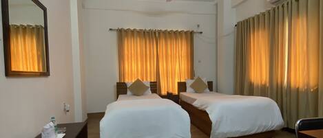 A hotel room with two beds, a ceiling fan, a desk with a chair, and a large mirror on the wall.