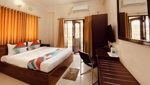 Habitación de hotel con cama, escritorio, silla, televisor y aire acondicionado.