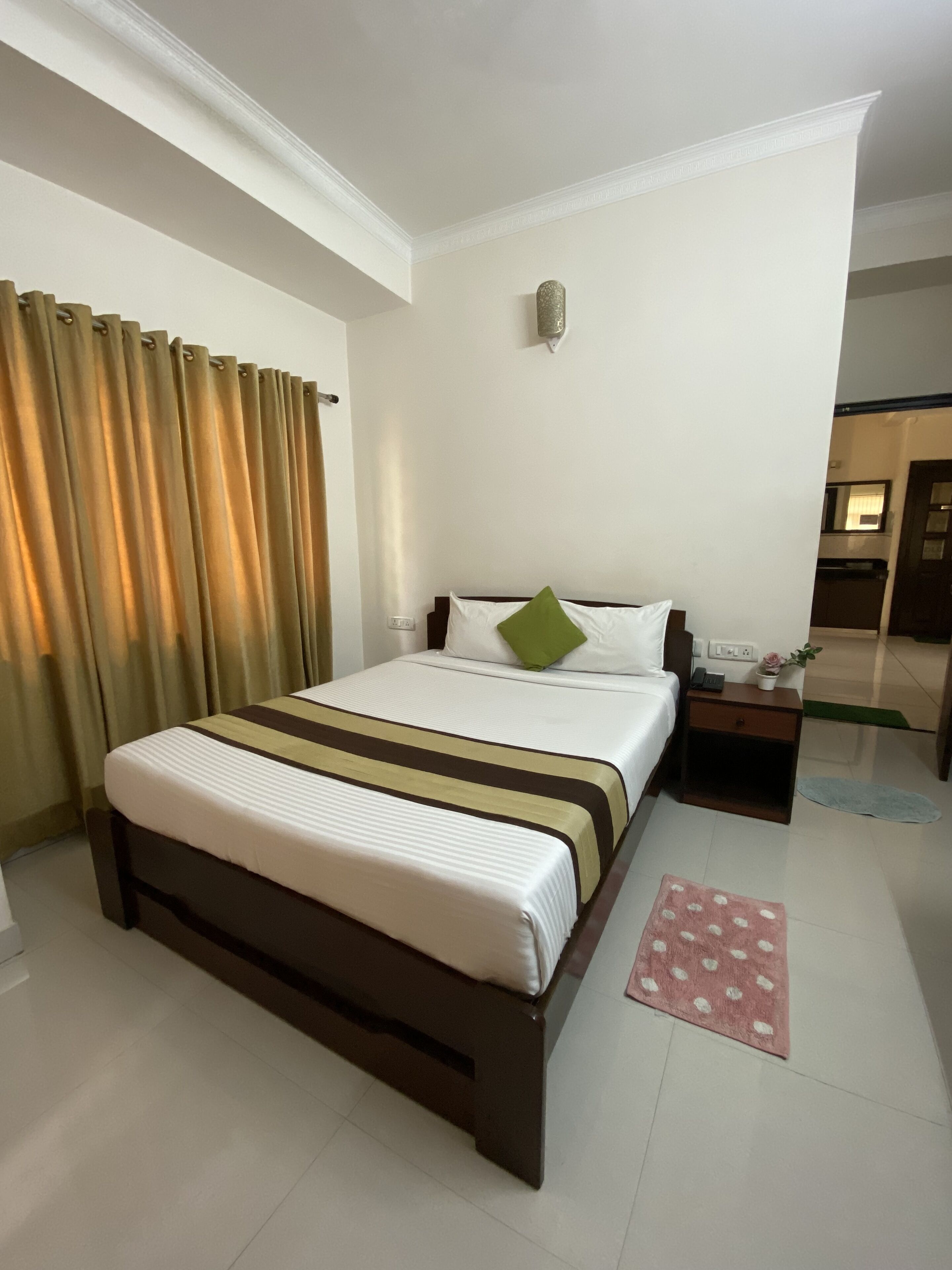 A hotel room with a large bed, a nightstand, a mirror, and a view of the hallway.