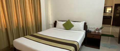 A hotel room with a large bed, a nightstand, a mirror, and a view of the hallway.