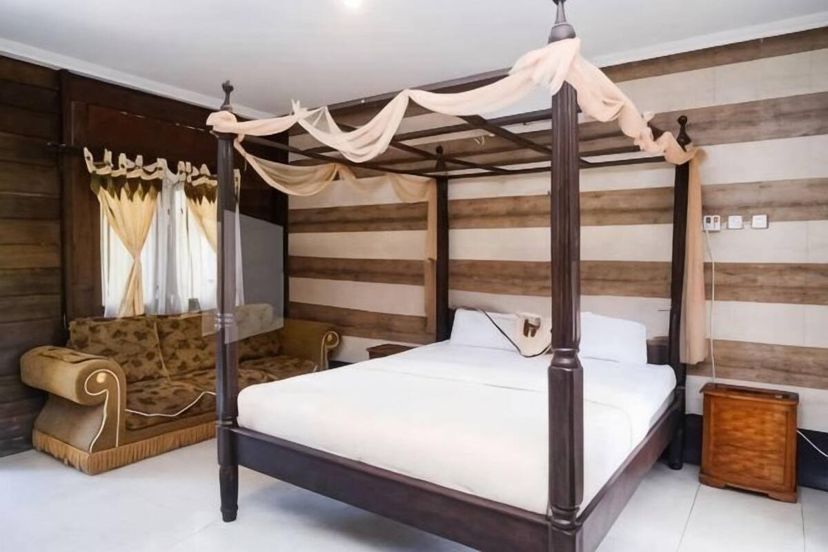 Una cama con dosel, un sofá y un aparador de madera en una habitación con paneles de madera.