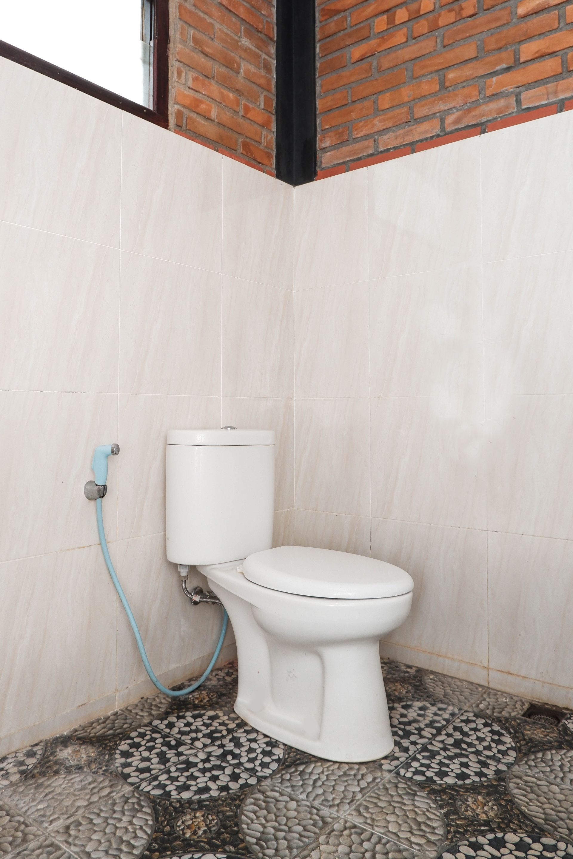 Baño con inodoro blanco, manguera azul y baldosas de suelo estampadas.