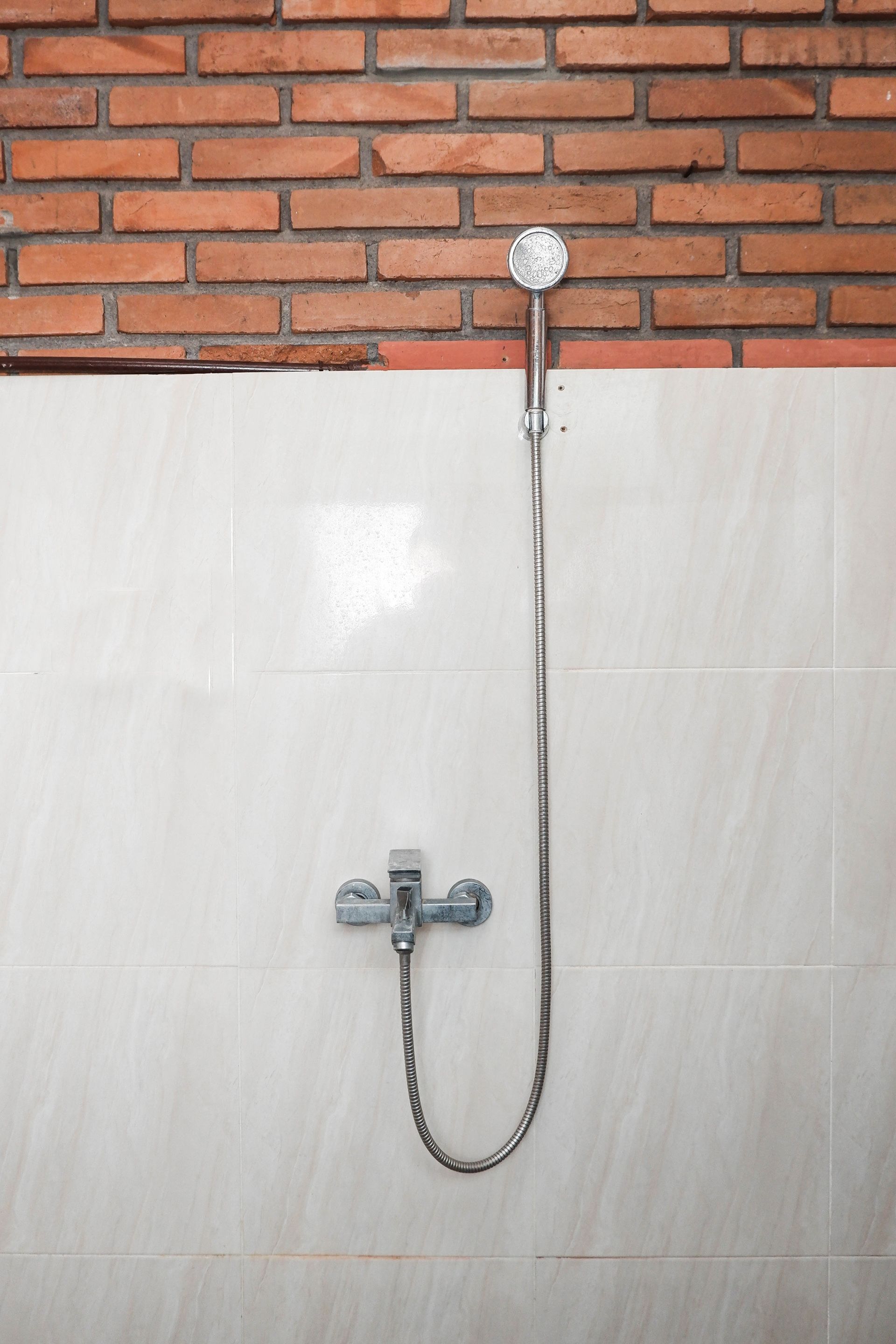 A shower with a hose and a handheld showerhead mounted on a tiled wall with a brick pattern.