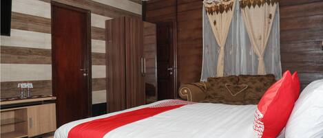Habitación de hotel con cama, armario de madera, escritorio con espejo y ventana con cortinas.