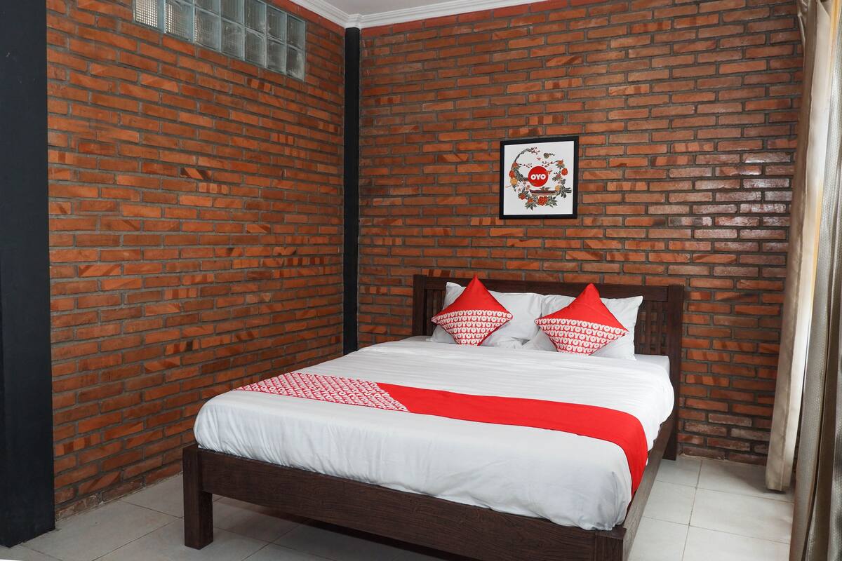 Een slaapkamer met een bakstenen muur, een bed met witte beddengoed en rode accenten, en een ingelijst kunstwerk aan de muur.