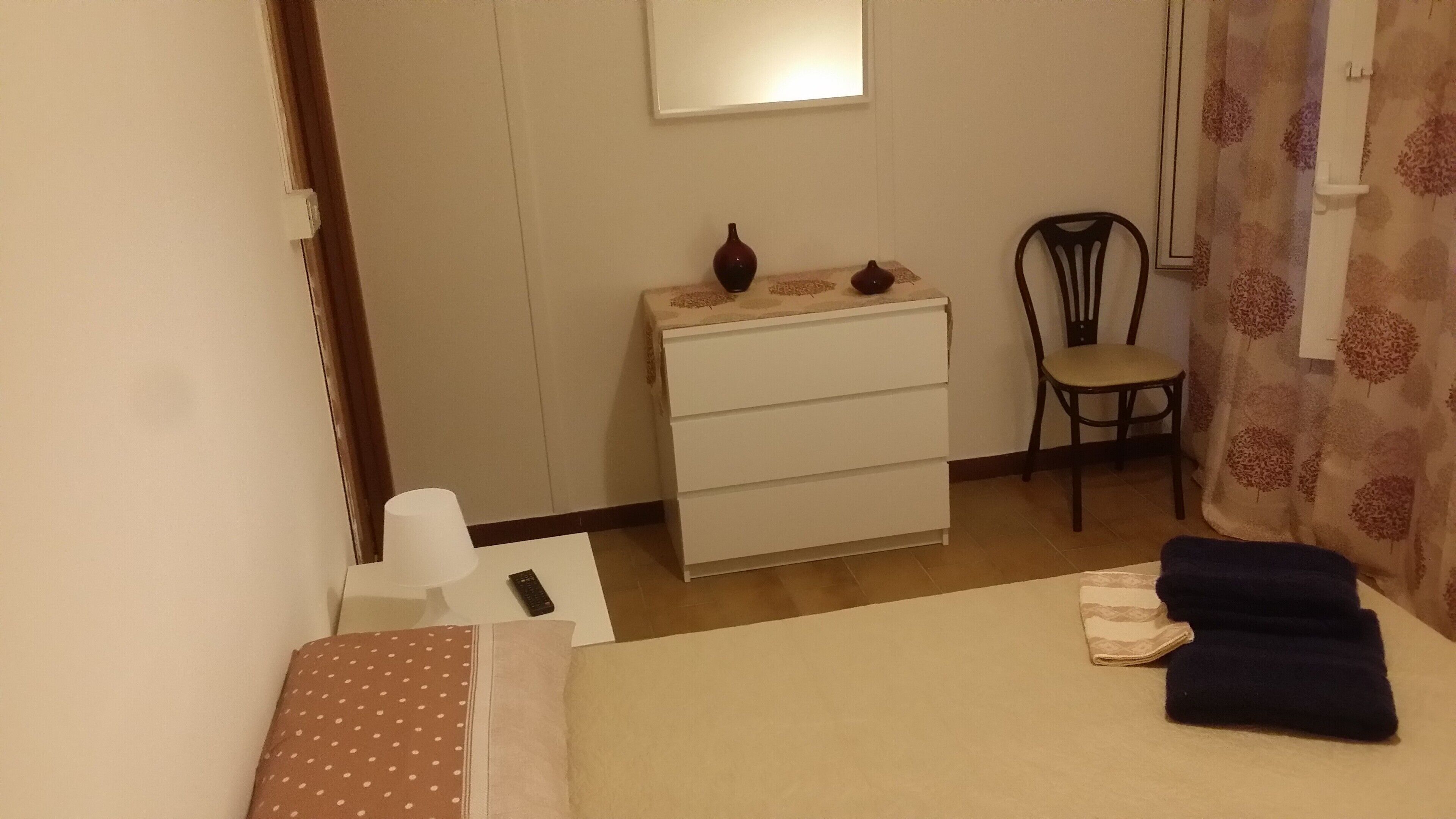 A small, neatly arranged bedroom with a bed, a dresser, a chair, and a nightstand.