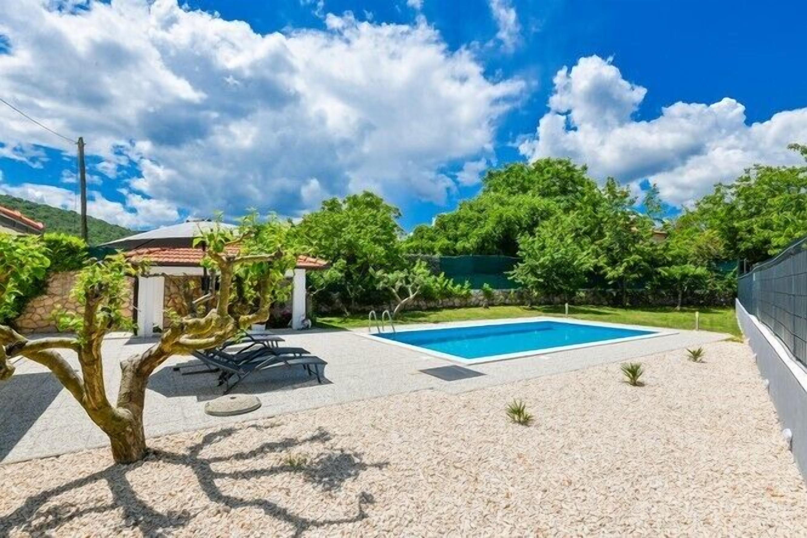 A backyard with a swimming pool, surrounded by greenery and a stone wall.