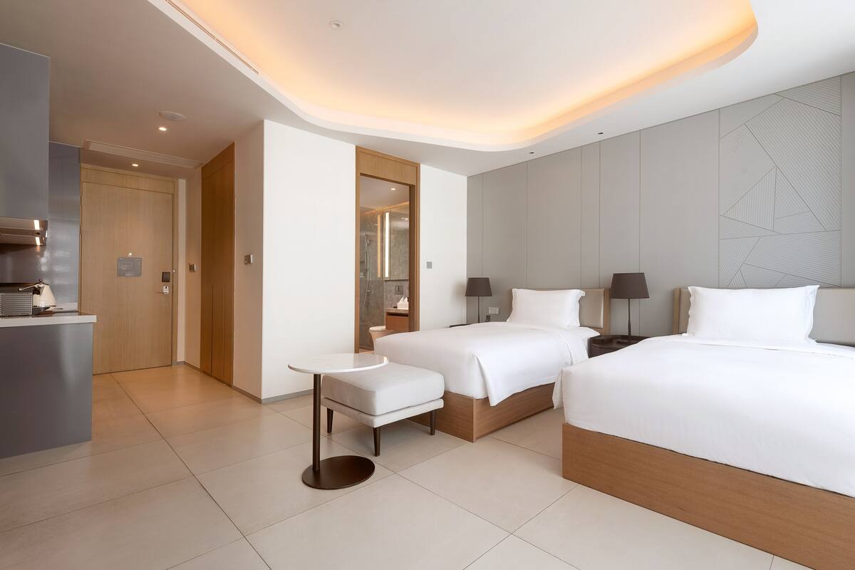 Une chambre d’hôtel moderne équipée d’un grand lit, de deux petits lits, d’un bureau et d’un miroir.