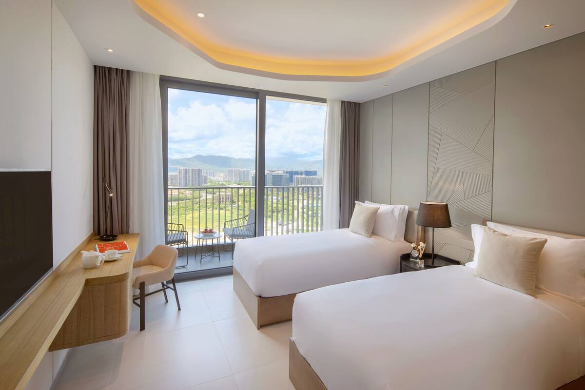 Une chambre d’hôtel avec deux lits, un bureau, une chaise et une grande fenêtre donnant sur la ville.
