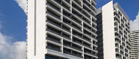 Un hotel moderno con un llamativo letrero vertical, varios balcones y un área de entrada ajardinada.