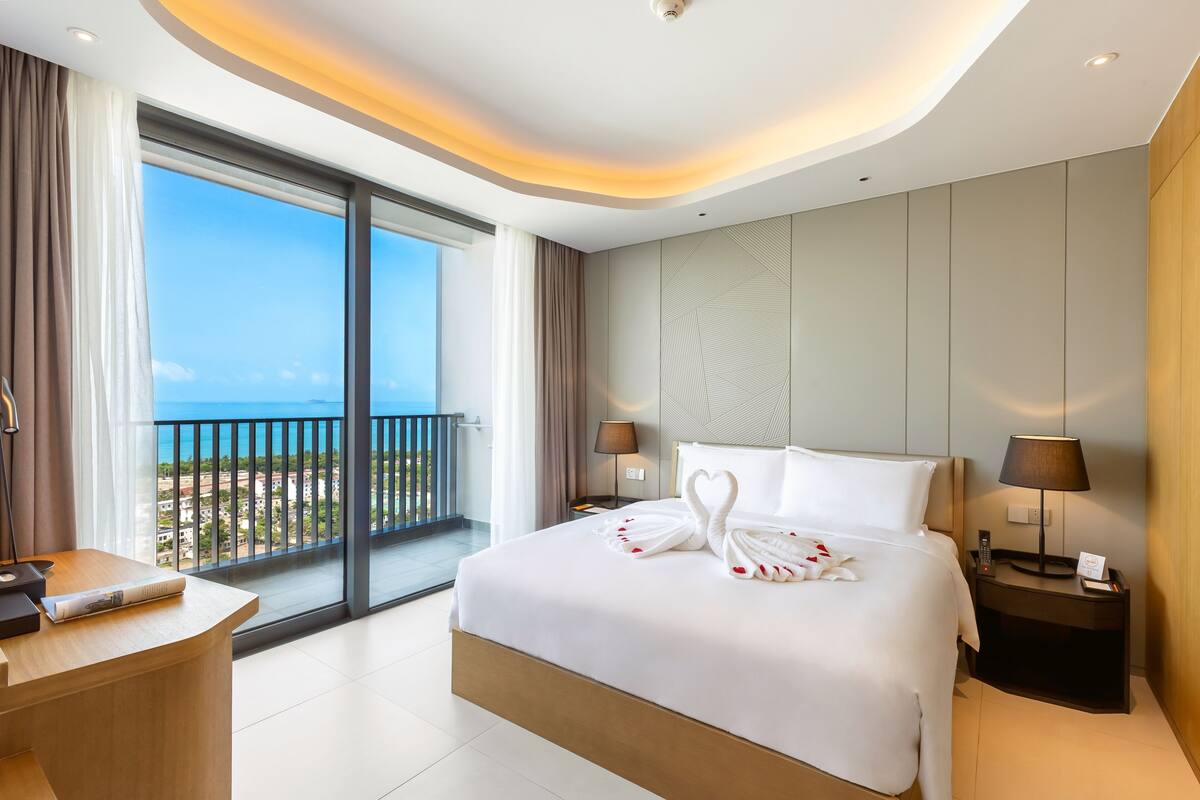 Une chambre d’hôtel moderne dotée d’un grand lit, d’un bureau, d’une table de chevet et offrant une vue sur la mer.