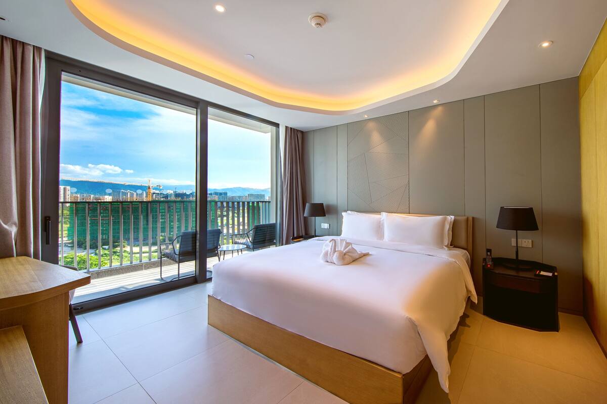 Une chambre d’hôtel moderne, dotée d’un grand lit, d’un bureau et offrant une vue sur le paysage urbain.