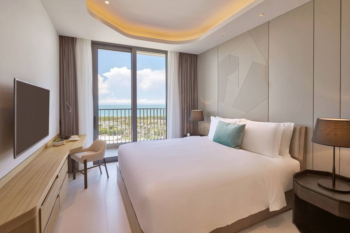Une chambre d’hôtel moderne dotée d’un grand lit, d’un bureau, d’une télévision et d’un balcon offrant une vue sur la ville.