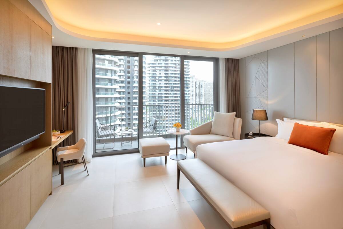 Une chambre d’hôtel moderne dotée d’un grand lit, d’un bureau, d’une télévision et d’un balcon offrant une vue sur la ville.