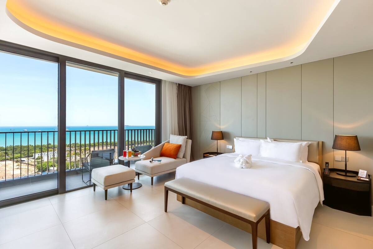 Une chambre d’hôtel moderne dotée d’un grand lit, d’un coin salon avec vue sur la mer et d’un balcon avec une balustrade.