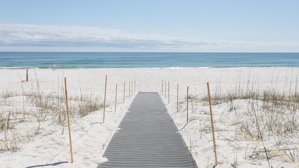 A wooden boardwalk leading to a beach with a clear sky. - Sundown B 34 (Pensacola)