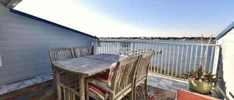 A balcony with a wooden table and chairs, a potted plant, and a view of the water.