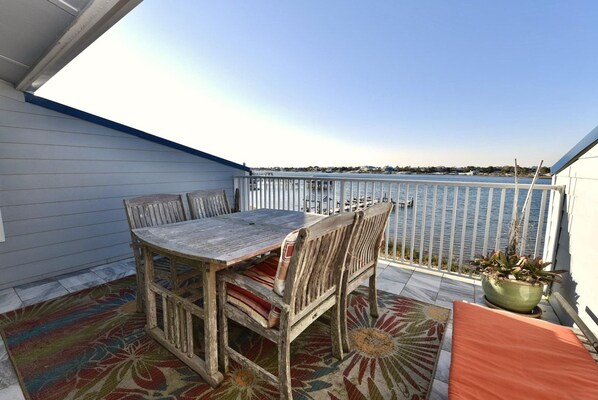 A balcony with a wooden table and chairs, a potted plant, and a view of the water.