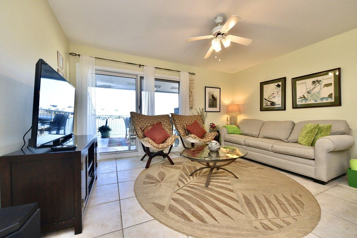 A living room with a sofa, two armchairs, a coffee table, a television, and a ceiling fan.