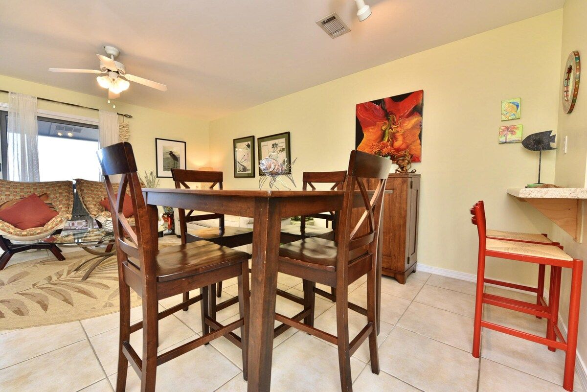 A dining area with a table and chairs, a ceiling fan, and artwork on the walls.