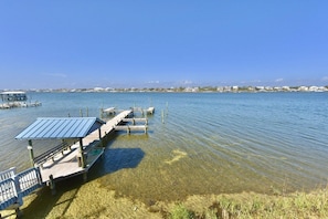 A clear waterfront view with a dock extending into the water, a covered seating area, and a distant shoreline with buildings. - B 34 Sundown Condominiums (Pensacola)