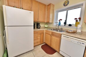 A kitchen with wooden cabinets, a white refrigerator, a dishwasher, and a window with flowers.