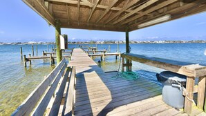 A wooden pier extending into calm water with a clear view of distant buildings. - Sundown B 34 (Pensacola)