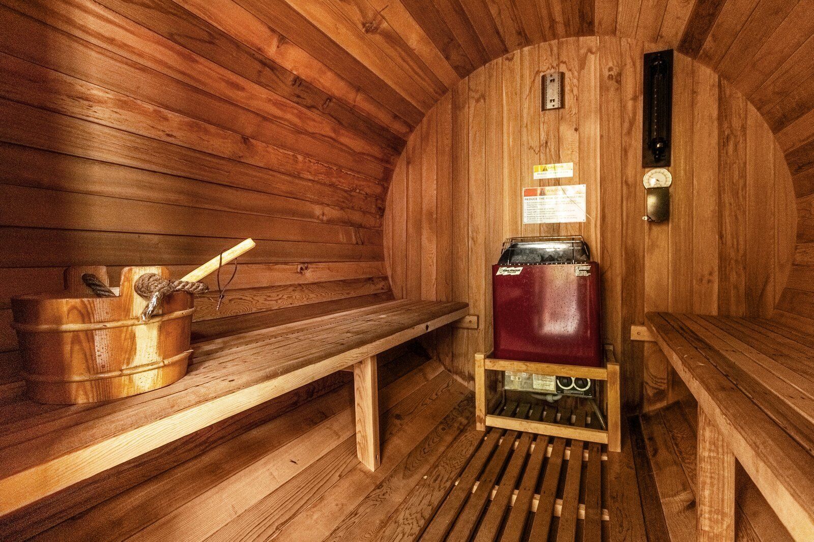 A sauna with wooden walls, a bench, a bucket with a rope, and a sauna heater.
