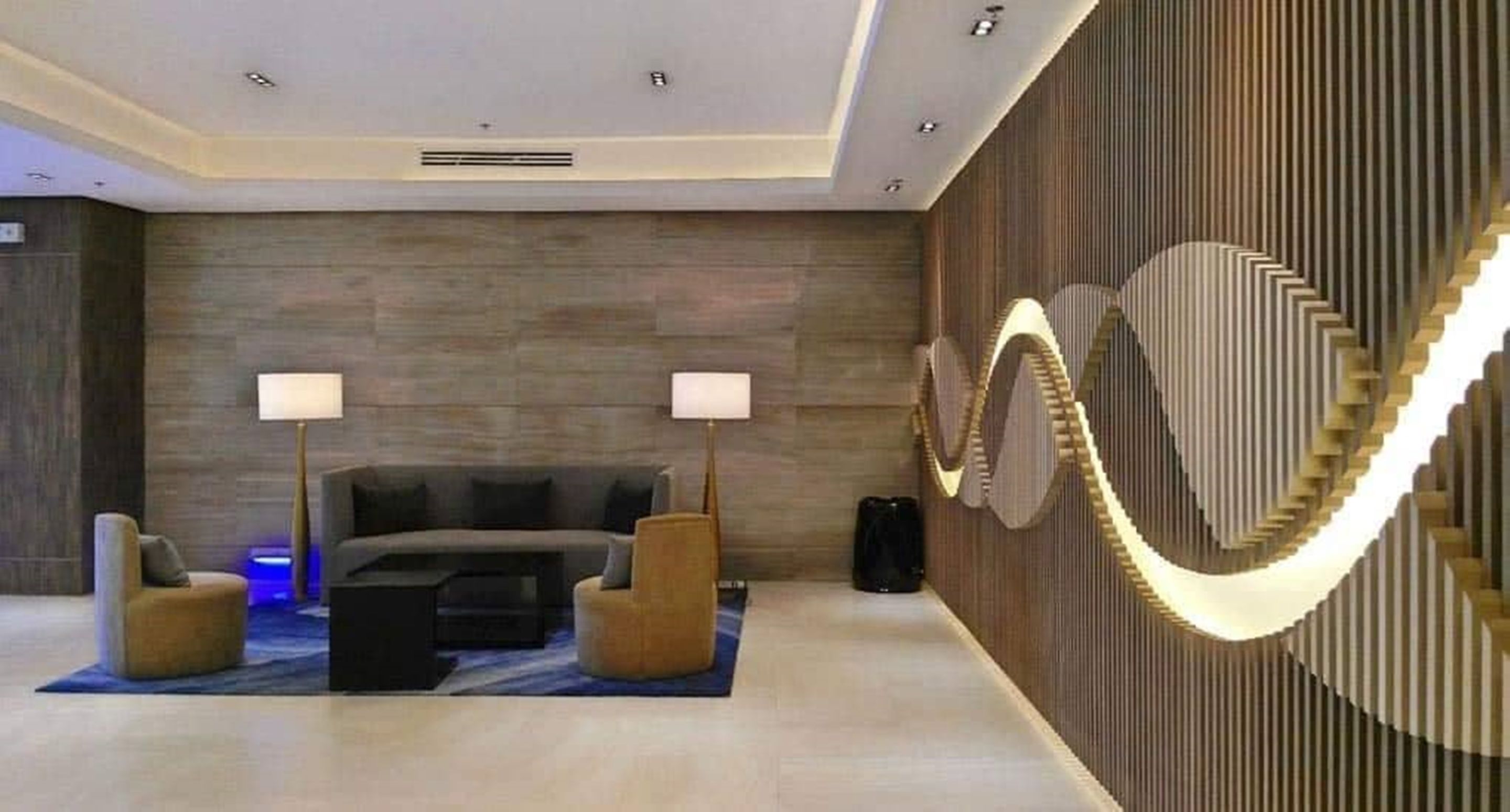 A modern hotel lobby with a sofa, two lamps, a coffee table, and a unique wall design.