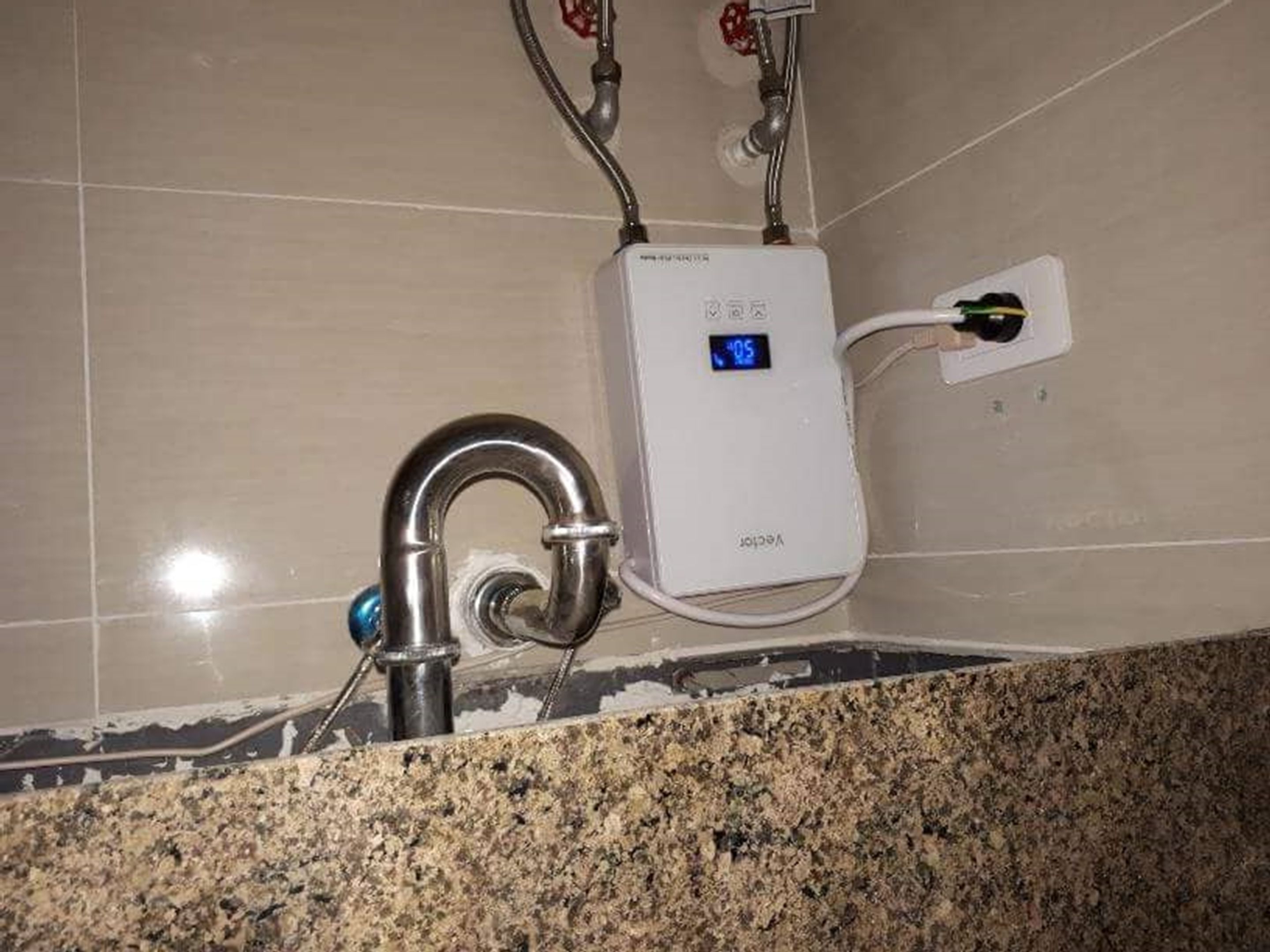 A bathroom with a digital water heater, a faucet, and a tiled wall.
