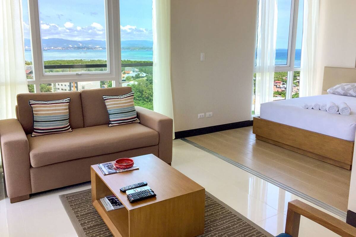 A modern hotel room with a sofa, a coffee table, a bed, and a view of the sea.