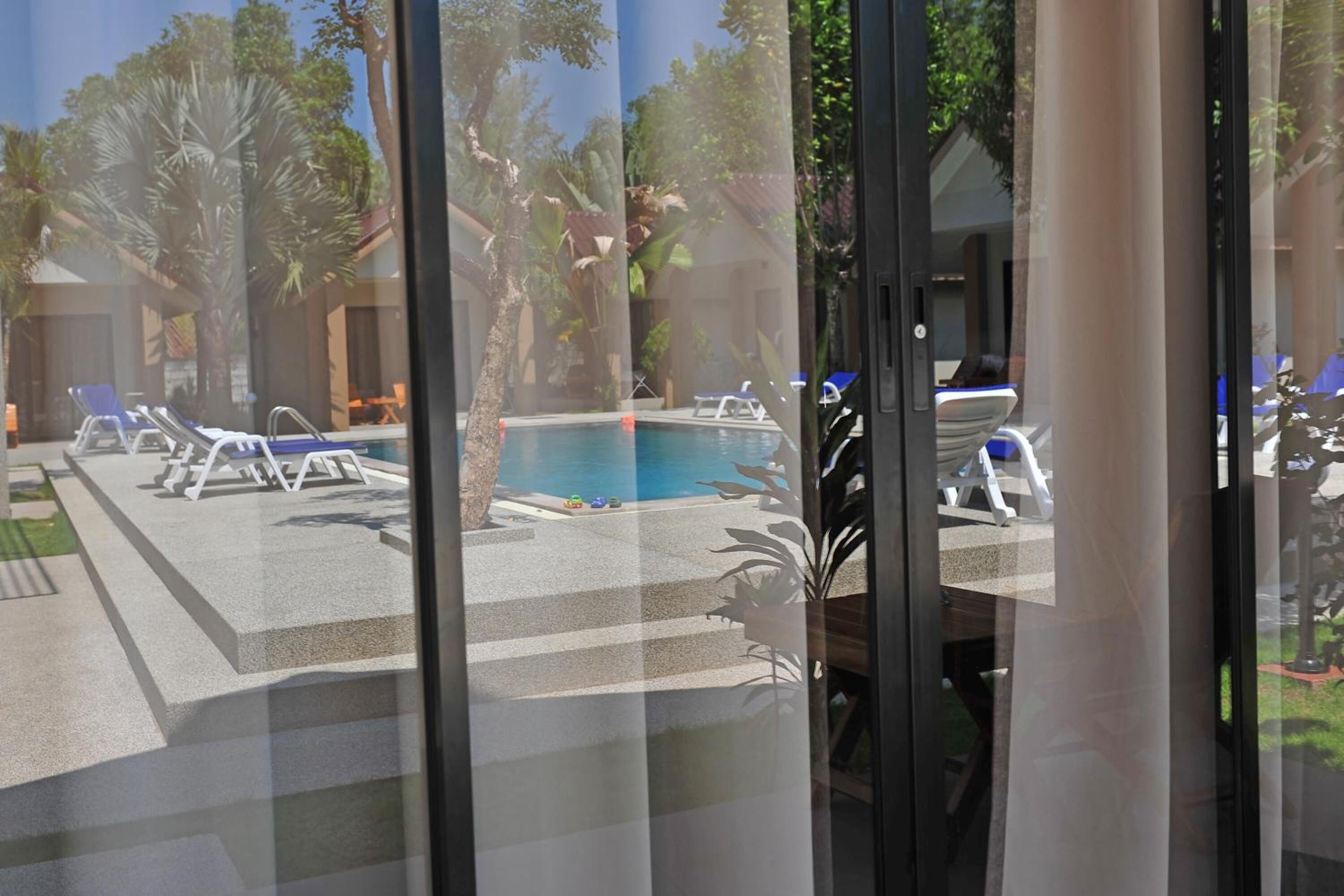 Un área de piscina con sillones y una alberca, rodeada de palmeras y un edificio.