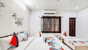 Una habitación de hotel con dos camas, cada una con ropa de cama de colores, una ventana con cortinas, un equipo de aire acondicionado y una puerta con un panel de madera.