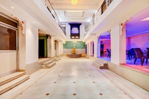 Un couloir d’hôtel avec une fontaine centrale, des marches menant à un balcon et un espace détente avec des tables et des chaises.
