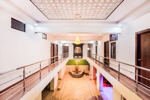 Passadís d'hotel de diversos nivells amb un penjoll central, una paret decorativa i una escala.